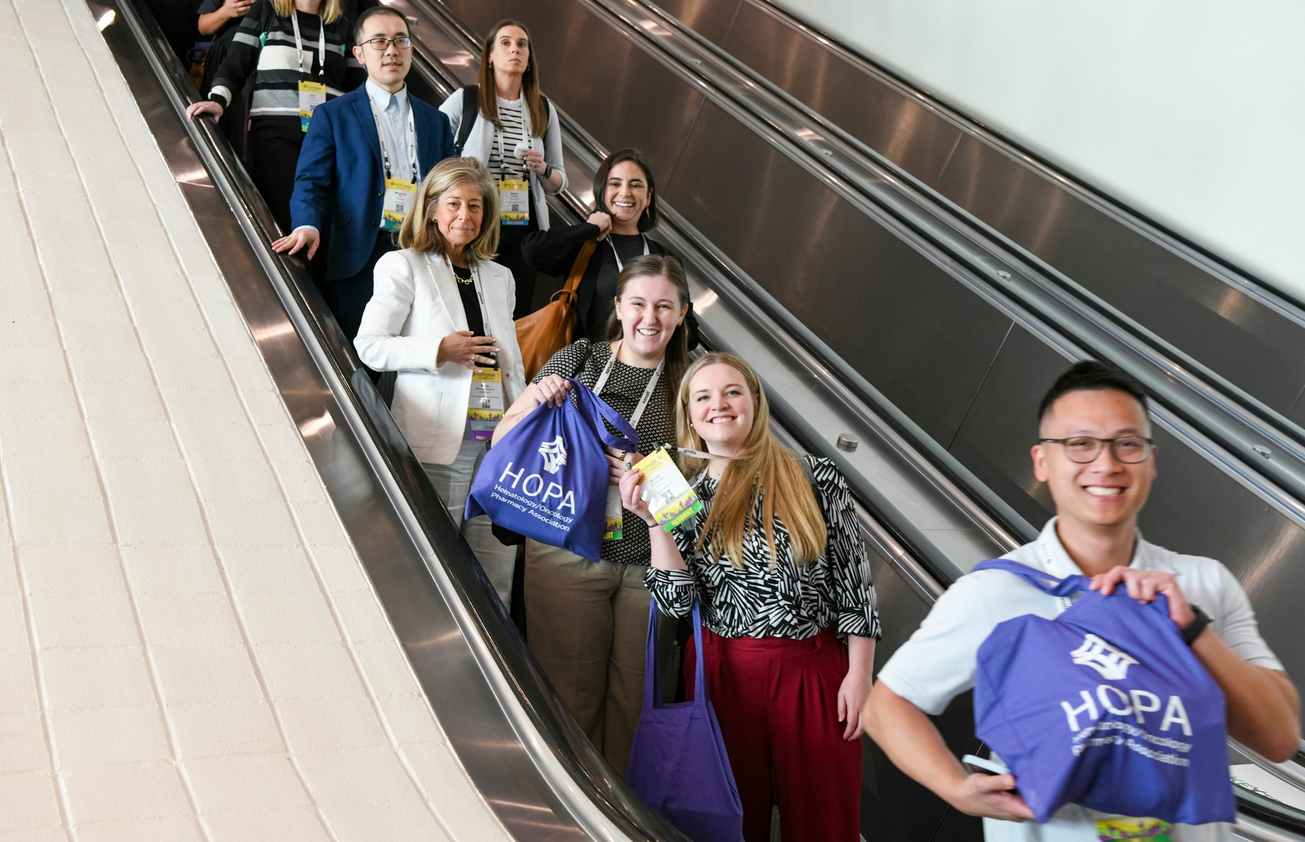 HOPA attendees holding up bags on an escalator