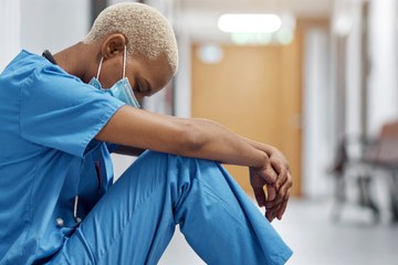 Nurse sitting in hospital hallway resting against a wall