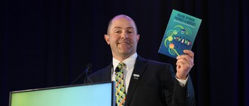 Robert Mancini speaking at HOPA 2026 while holding a copy of the HOPA Book of Letters