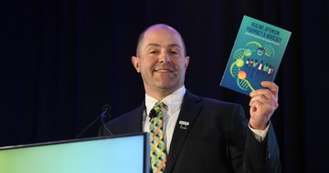 Robert Mancini speaking at HOPA 2026 while holding a copy of the HOPA Book of Letters