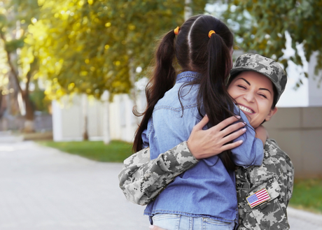Latina in military fatigues hugging her school-aged daughter